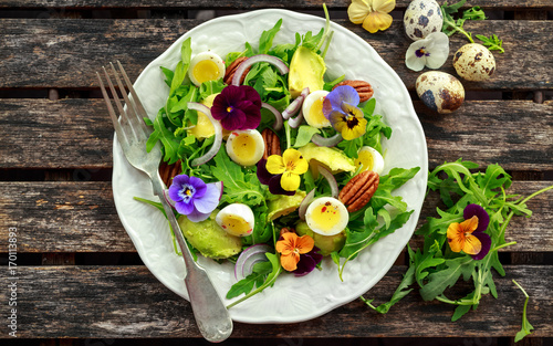 Healthy summer salad with quail eggs, avocado, pecans, wild rocket, red onion and edible viola flowers.