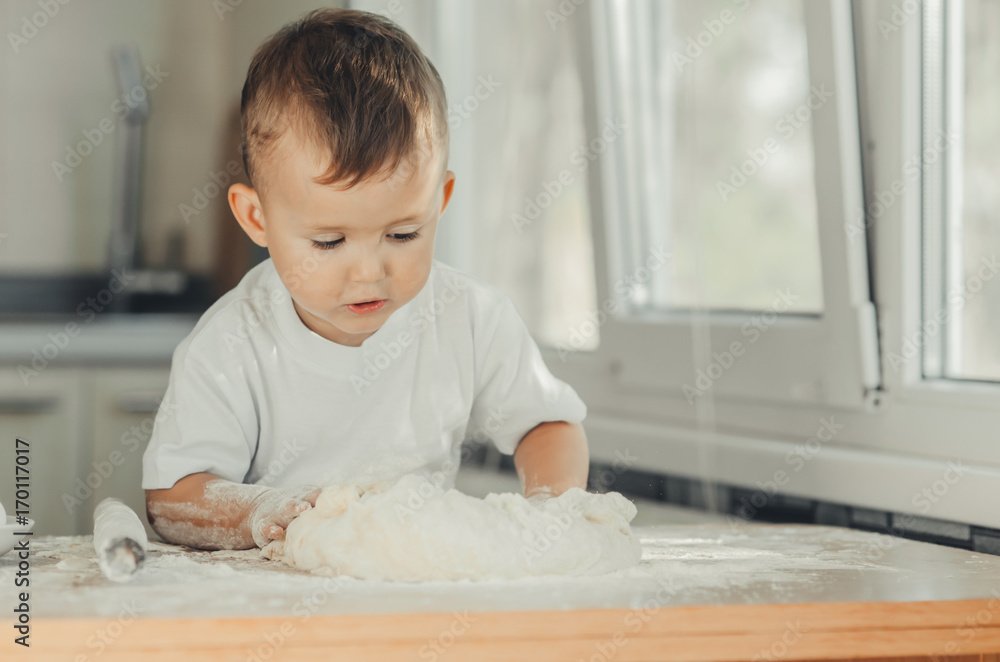 Fototapeta premium The little Boy in the kitchen hard kneads the dough