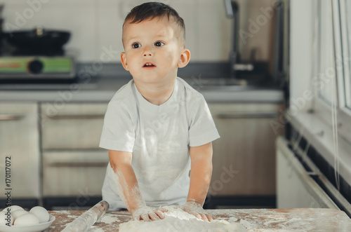 The little Boy in the kitchen hard kneads the dough photo