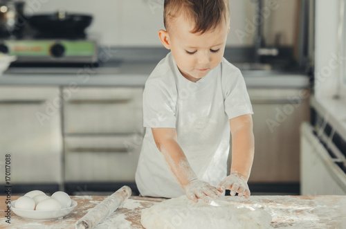 The little Boy in the kitchen hard kneads the dough photo