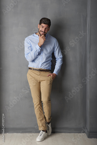 Handsome young man portrait. Full length studio shot of a young man wearing casual clothes while standing at grey wall.