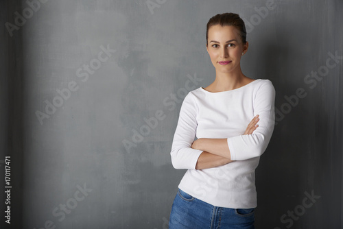 Attractive young woman portrait. Portrait shot of a beautiful young woman standing with arms crossed at grey wall.