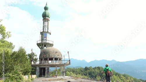 Tourist walking at abandoned minaret Arabian style, destroyed building in Consonno, Italy. Man hiking at ghost town construction with graffiti and wild vegetation, desolate and scary place photo