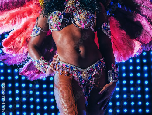 Beautiful bright colorful carnival costume illuminated stage background. Samba dancer hips carnival costume bikini feathers rhinestones close up.