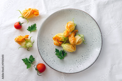 Zucchini (courgette) flowers on plate. Healthy summer food. Top view. Fresh vegetables decoration.