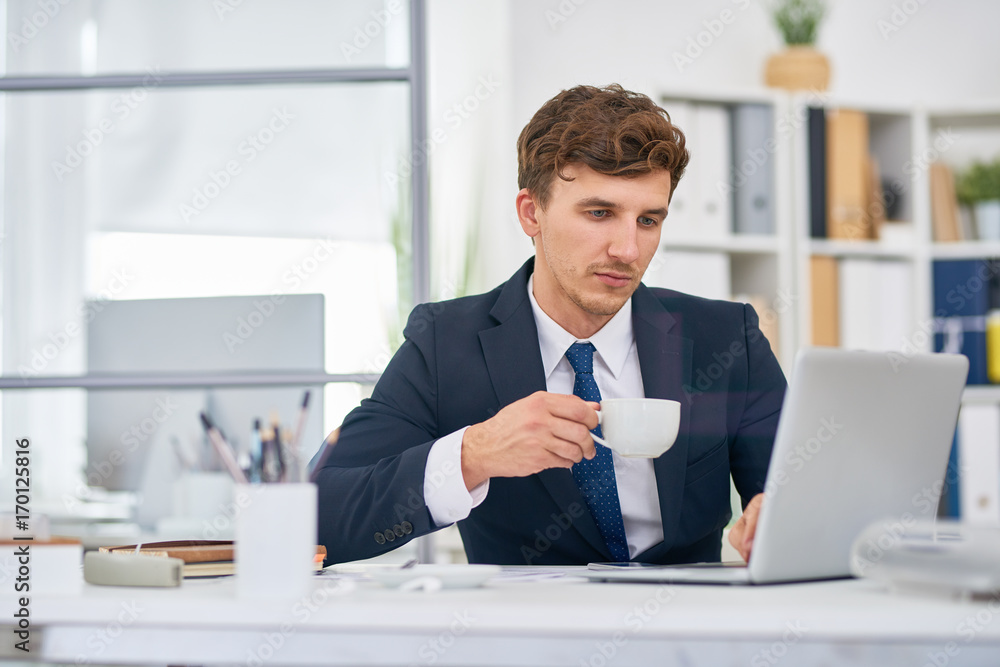 Portrait of modern businessman working in office drinking coffee at desk and using laptop Portrait of modern businessman working in office drinking coffee at desk and using laptop