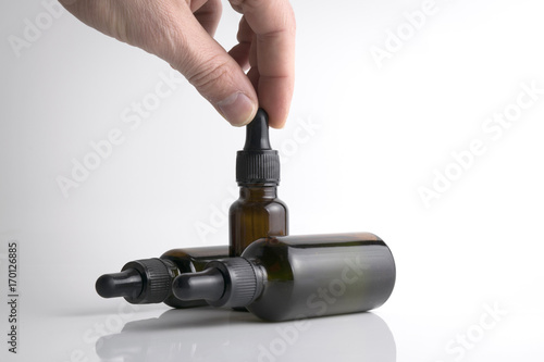 Isolated hand holding a medical brown drop bottle over a white b