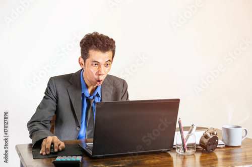 A young businessman wearing a suit was shocked when he looked at a laptop on a desk in his office, business people concept.