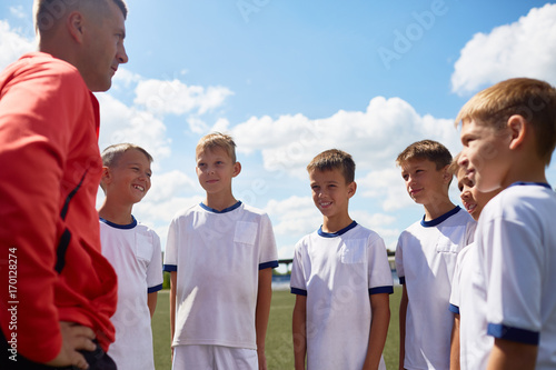 Portrait of smiling football players listening to coach in field on sunny day