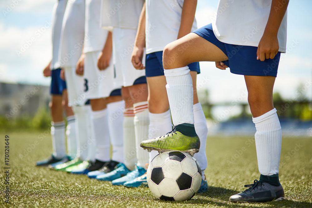 Fototapeta premium Low section portrait of junior football team : legs of boys standing in row with captain stepping on ball in foreground