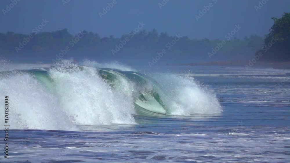 SLOW MOTION, CLOSE UP: Huge reef break wave rolling towards beautiful tropical sandy beach with palm trees on sunny Bali. Water drops splashing and shimmering. Foamy tube barrel crashing and spraying SLOW MOTION, CLOSE UP: Huge reef break wave rolling towards beautiful tropical sandy beach with palm trees on sunny Bali. Water drops splashing and shimmering. Foamy tube barrel crashing and spraying