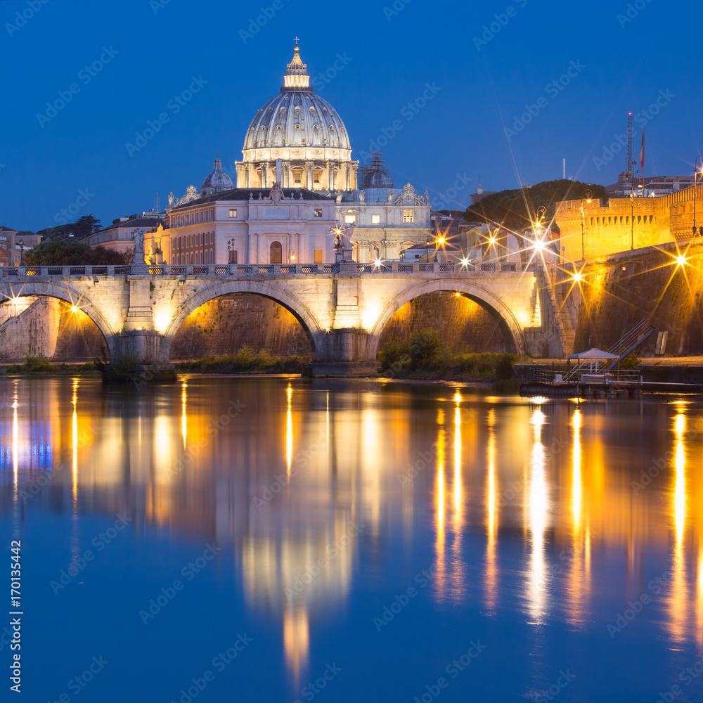 Saint Angel bridge and Saint Peter Cathedral with a mirror reflection in the Tiber River during morning blue hour in Rome, Italy.
