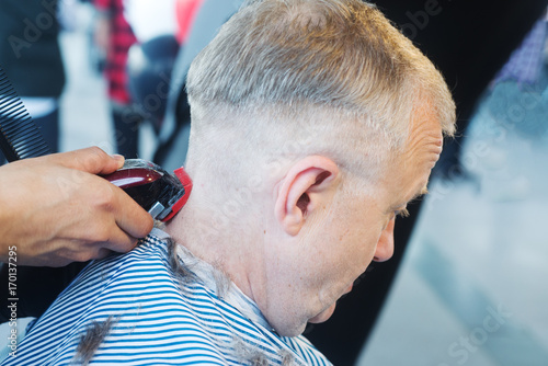 Barber working with electric razor in barbershop for handsome man