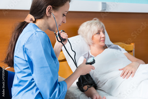 Wallpaper Mural Attractive female nurse in uniform with phonendoscope is measuring the arterial pressure of her patient using a medical equipment Torontodigital.ca