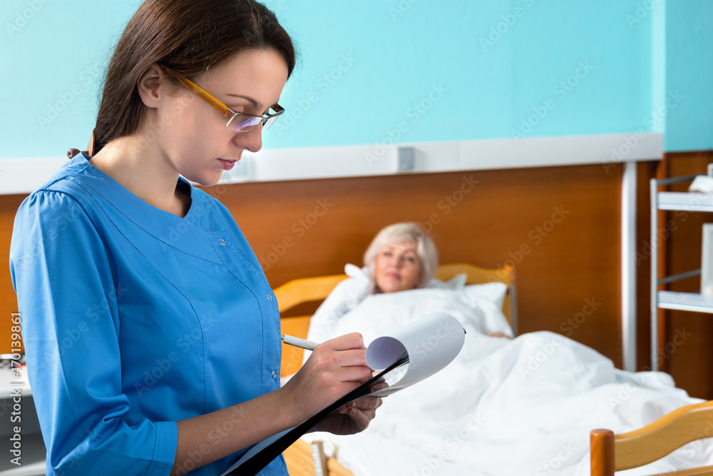 Attractive nurse in uniform wearing a mask and glasses making some notes in report at clipboard Attractive nurse in uniform wearing a mask and glasses making some notes in report at clipboard
