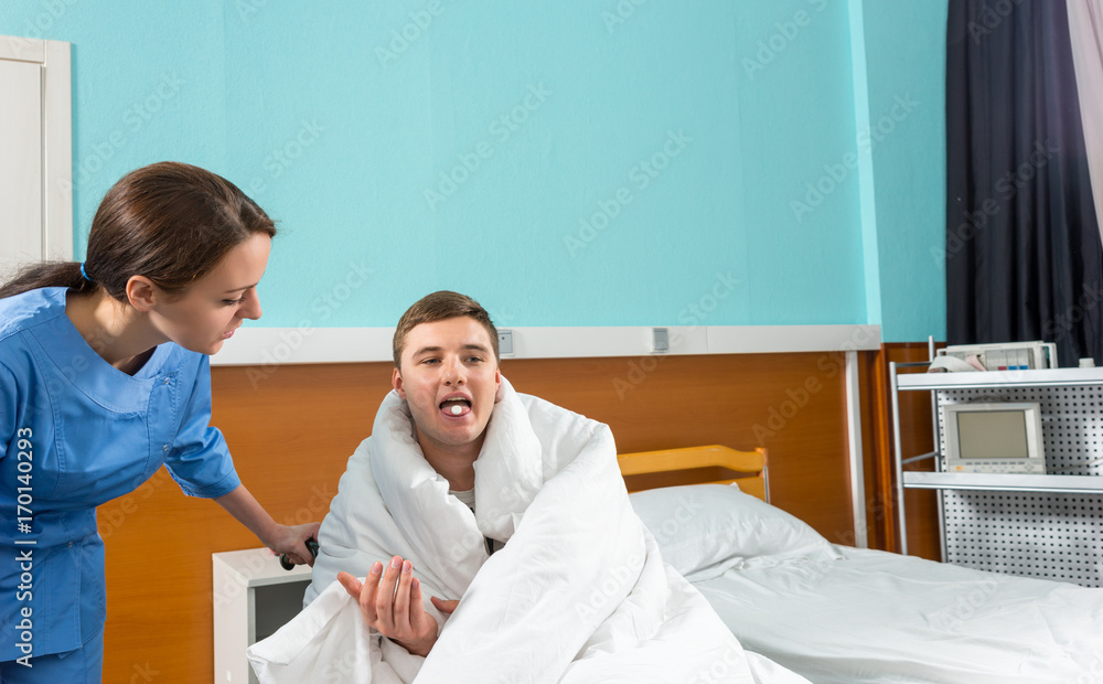 Fototapeta premium Beautiful nurse giving pills to ill patient sitting on wheelchair covered with quilt in hospital ward