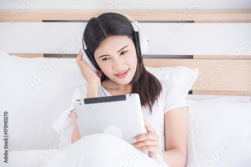 Beautiful asian woman listening music via headphone while sitting on bed