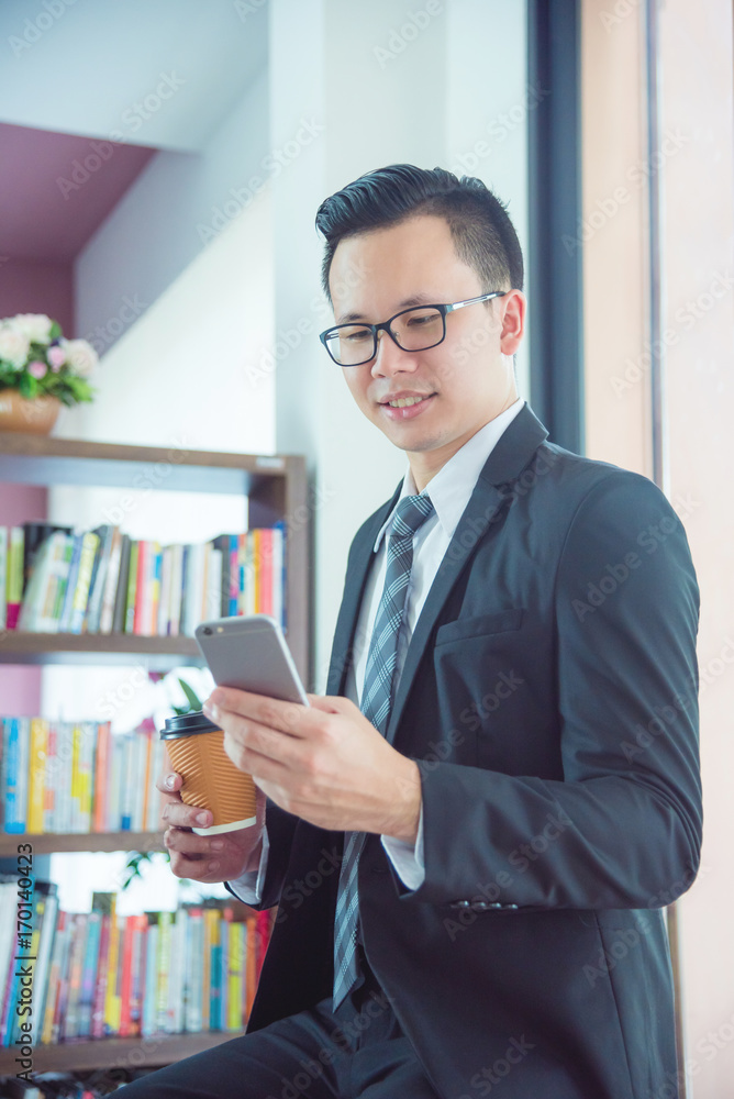 Young asian businessman holding coffee cup while using mobile phone in office Young asian businessman holding coffee cup while using mobile phone in office