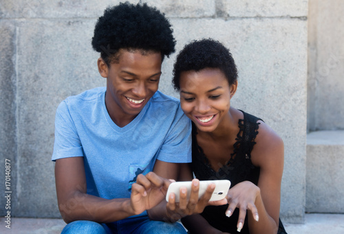 Joyful laughing african american couple looking at phone