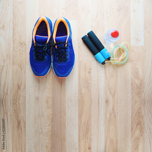 Sneakers next to a skipping rope and a bottle of water. Top view. Wooden floor and empty copy space for Editor's text.