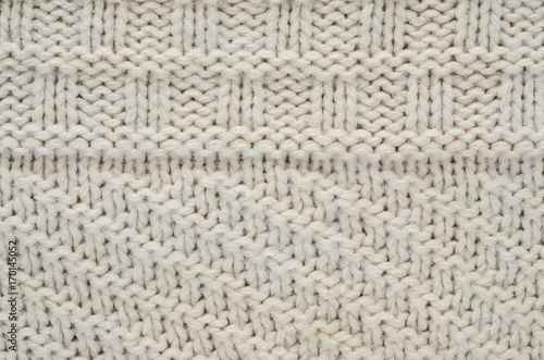 The texture of a knitted sweater is a thick beige string. Part of a sweater with various kinds of patterns close-up