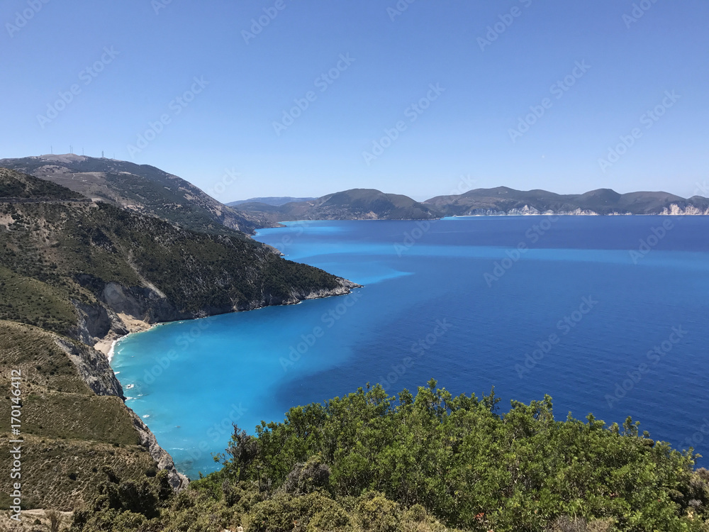 The coast of Kefalonia in Greece with its turquoise sea, blue sky and green mountains.