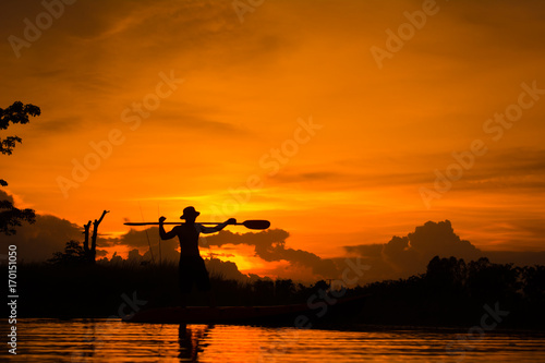 Silhouette of fisherman standing on boat,hold paddle,on sunset background.