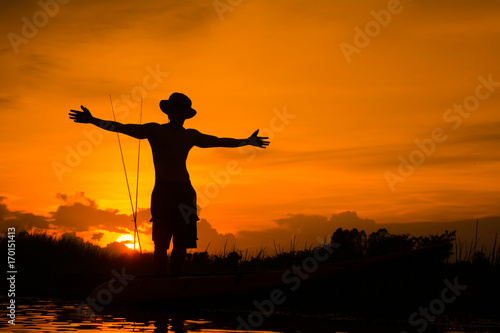 Silhouette traveler man relaxing on the beach with fishing rod and raise hand him arms open felling freedom.