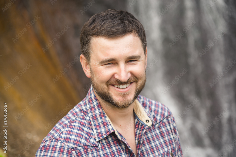 Close-up portrait of a bearded smiling hipster against a waterfall background Close-up portrait of a bearded smiling hipster against a waterfall background