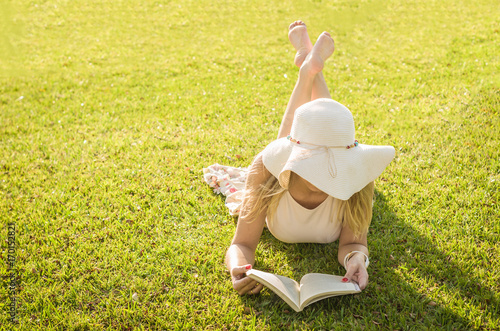 Linda mulher lendo um livro no gramado verde, sol de verão. photo