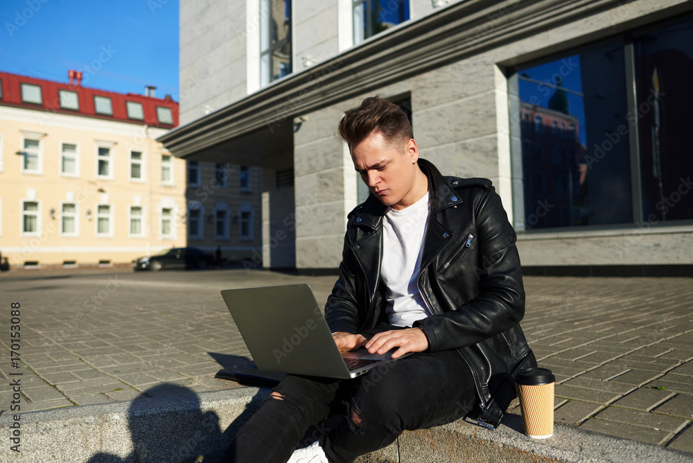People, technology, urban lifestyle and communication concept. Outdoor picture of serious concentrated college student in stylish black slothes sitting on steps and using generic web-enabled laptop People, technology, urban lifestyle and communication concept. Outdoor picture of serious concentrated college student in stylish black slothes sitting on steps and using generic web-enabled laptop