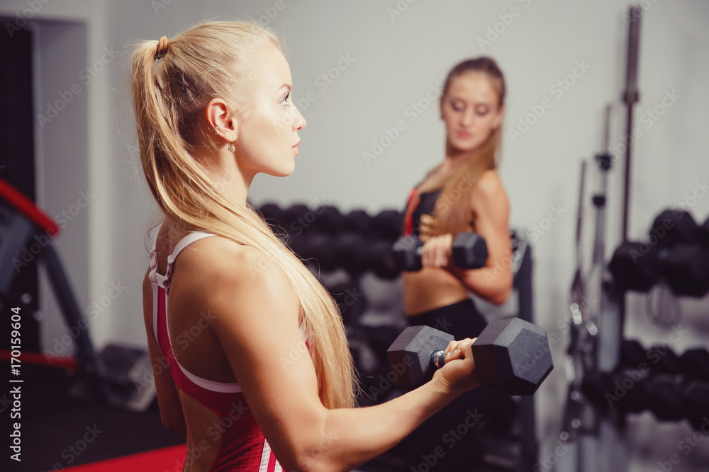 Woman exercising with a dumbbell in the gym, biceps exercising close-up, in the background a girl trains. copyspace Woman exercising with a dumbbell in the gym, biceps exercising close-up, in the background a girl trains. copyspace