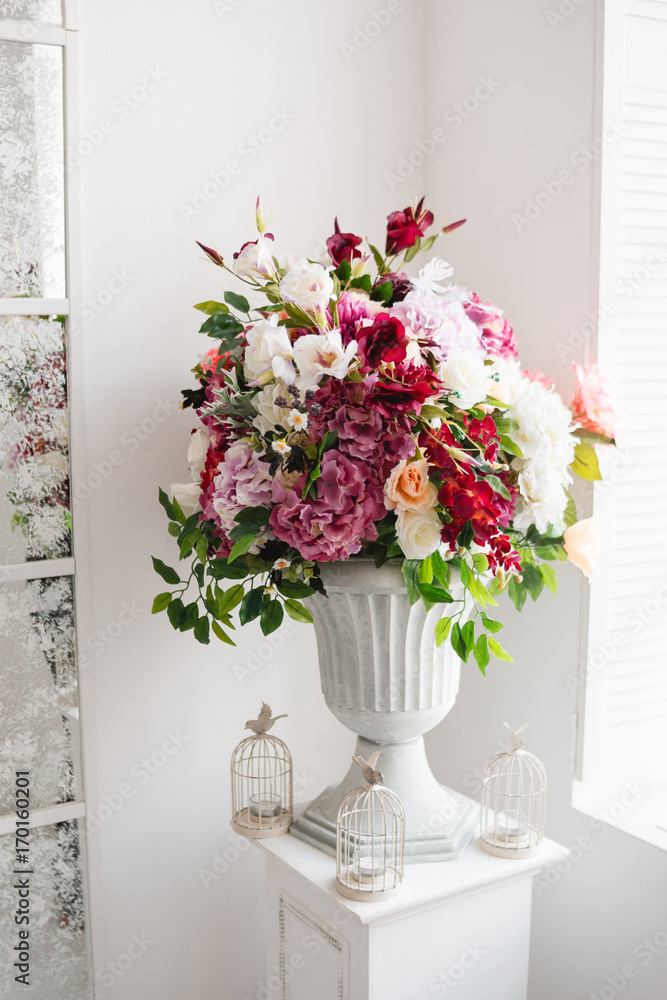 Fototapeta premium Beautiful flowers in classic white vase. Indoor decoration, gallery. Different colored roses, deep red eustoma, crimson hydrangea in rich blossomed bouquet
