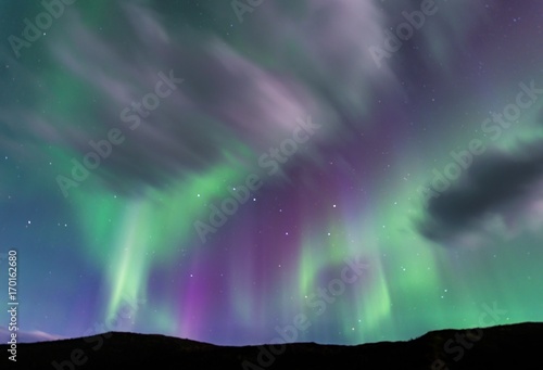 Purple and green Aurora borealis over silhouetted foreground with the Big Dipper prominently positioned in center of purple band