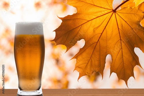 Фотография Glass of light Beer with foam against branch of maple with yellow leaves