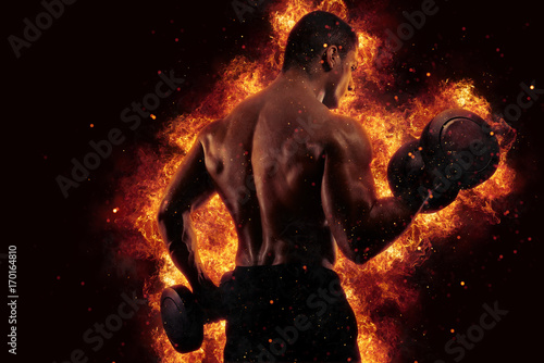 Athletic man training biceps at the gym with fire effect