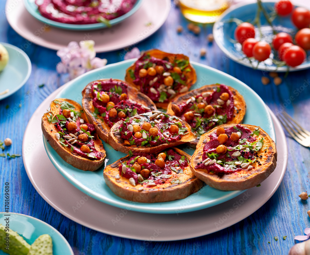 Sweet potato toast with beet hummus, grilled chickpeas, fresh parsley, nigella seeds and sunflower seeds on a plate on a blue table, top view. A nutritious and delicious vegan meal Sweet potato toast with beet hummus, grilled chickpeas, fresh parsley, nigella seeds and sunflower seeds on a plate on a blue table, top view. A nutritious and delicious vegan meal