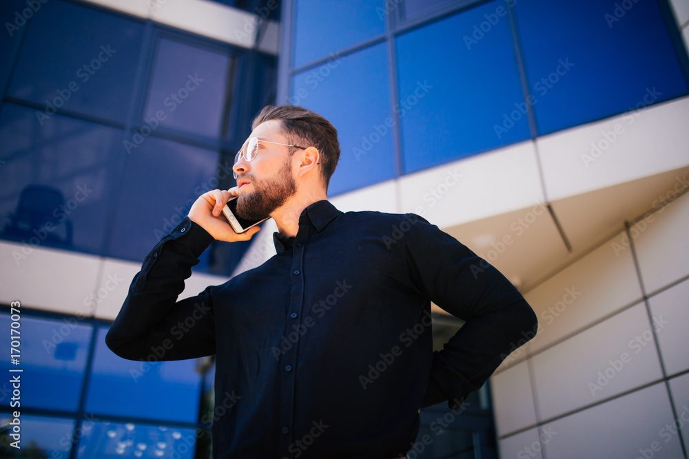 Portrait of handsome bearded businessman talking phone standing near office Portrait of handsome bearded businessman talking phone standing near office
