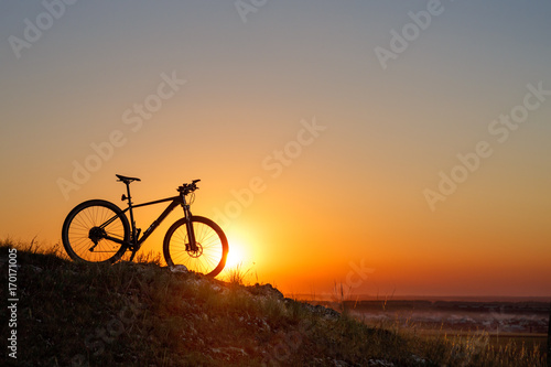 Silhouette of a bike on the hills at sunset. © Aleksey