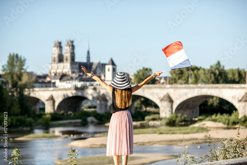 Young woman tourist standing back with french flag on the beautiful cityscape background during the sunset in Orleans, France photo