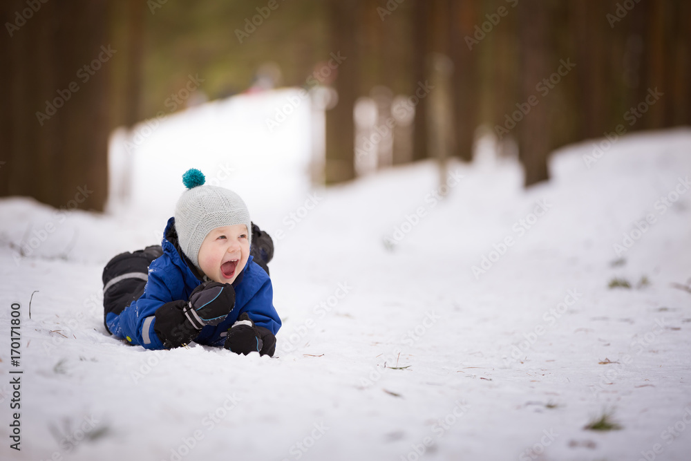 Portrait of cute toddler in warm winter clothes laying on the snow