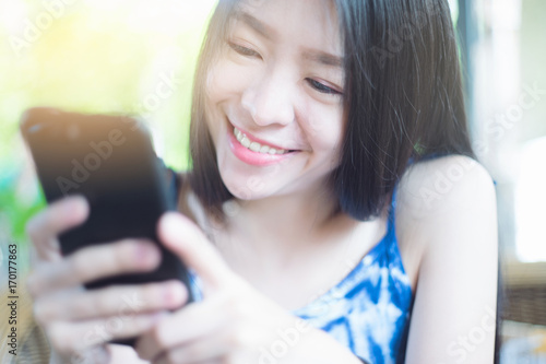 Portrait of young asian cute woman playing a smart phone and smiling. text for someone with happiness. in coffee cafe. selective focus. filtered image to vivid color tone process. light effect added