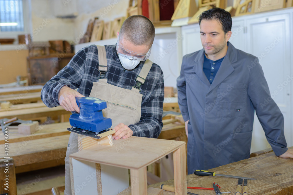 male apprentice sanding a cabinet part in a woodshop male apprentice sanding a cabinet part in a woodshop