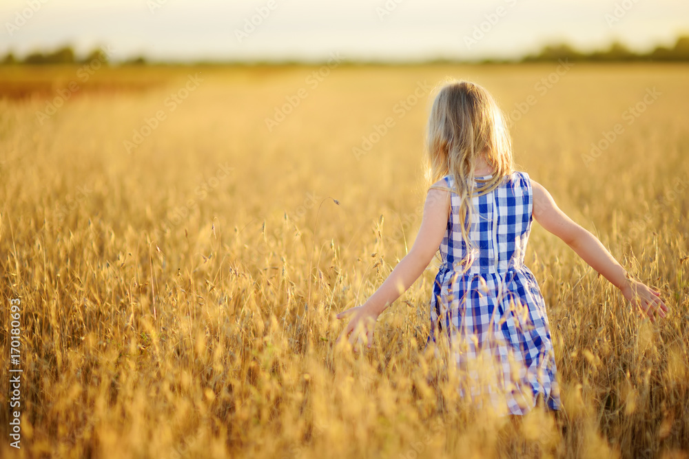 Adorable girl walking happily in wheat field on warm and sunny summer evening Adorable girl walking happily in wheat field on warm and sunny summer evening