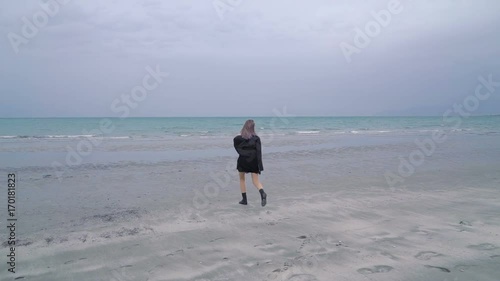 Happy beautiful blonde woman walks along the beach, cold rainy weather, autumn. Sexy girl hipster or punk, grunge in a black leather jacket is walking through puddles near the sea or ocean
