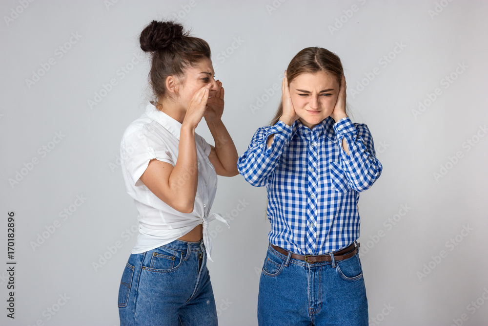 Young angry woman screaming and sulking sister closing her ears Young angry woman screaming and sulking sister closing her ears