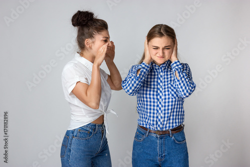Young angry woman screaming and sulking sister closing her ears
