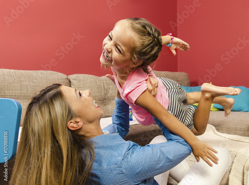 Adorable happy little girl flying throw air in her mothers arms. Mother holding her daughter in arms and laughing. 