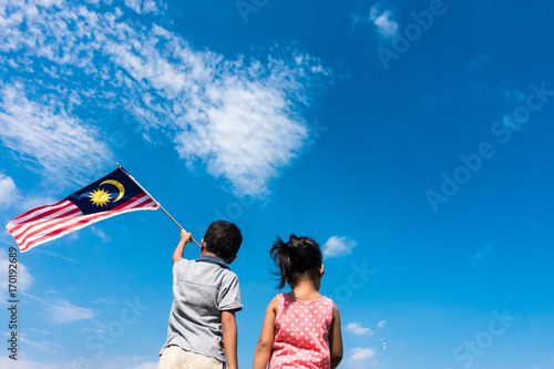 Unknown kids/brother and sister waving the Malaysia Flag. Independence Day & Merdeka Concept. Blue sky and copy space.