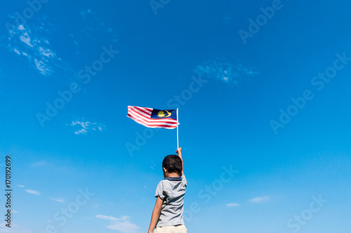 Unknown kid waving Malaysia Flag. Independence day and Merdeka Celebration. Blue sky and copy space. photo